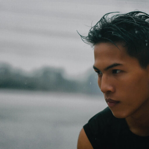 a young man with wet hair, wearing a black sleeveless shirt, in a moody, rainy outdoor setting.